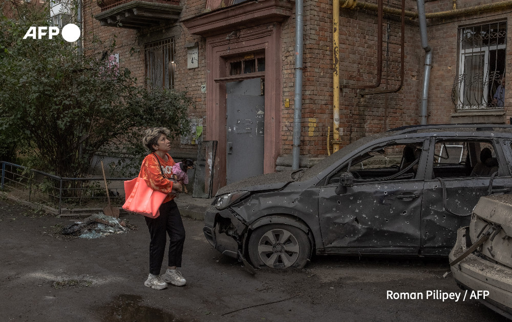 A woman holding a dog looks at cars and a residential building damaged following a Russian drone attack, in Kyiv amid the Russian invasion in Ukraine. 